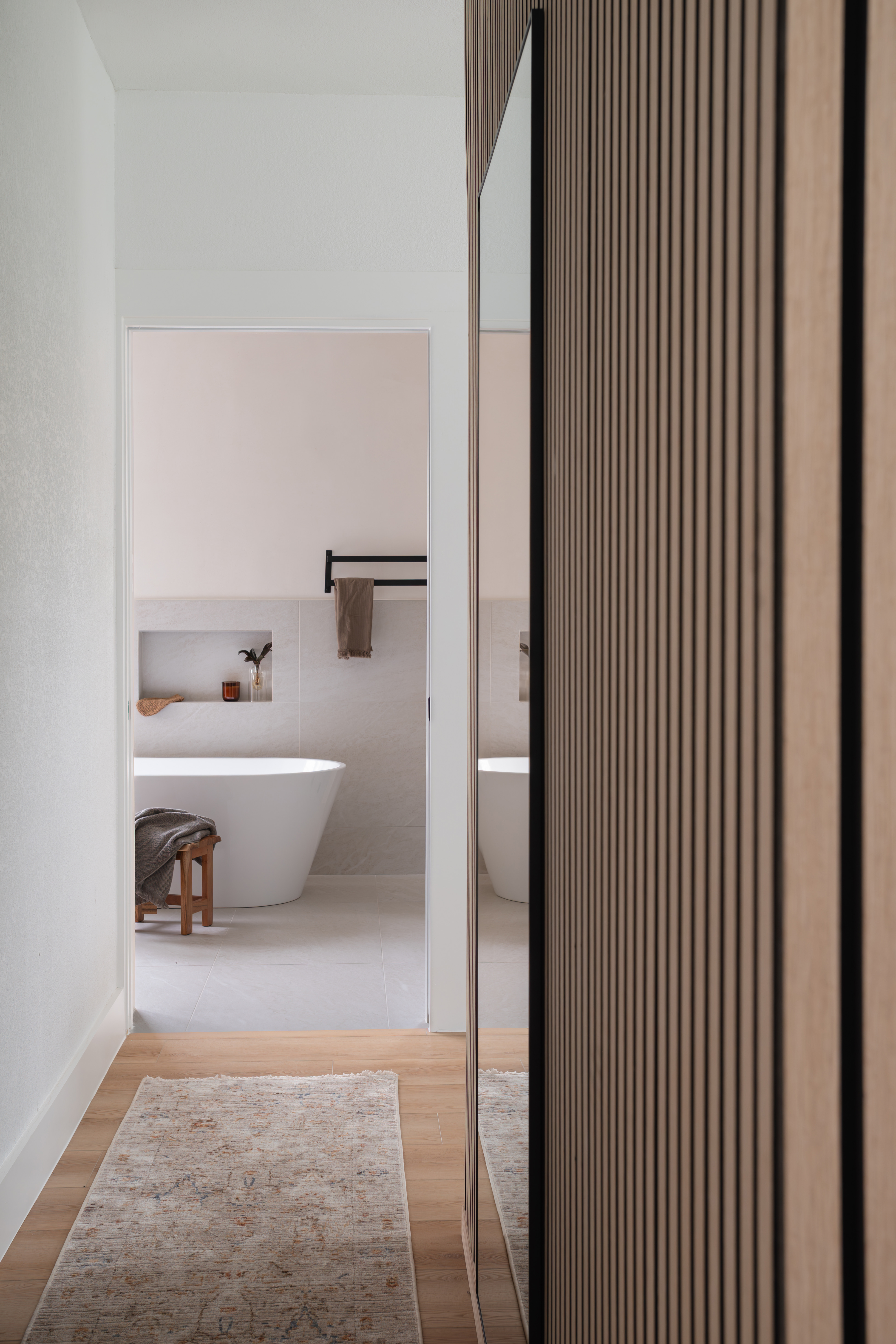 Hallway with slat wall leading to freestanding tub