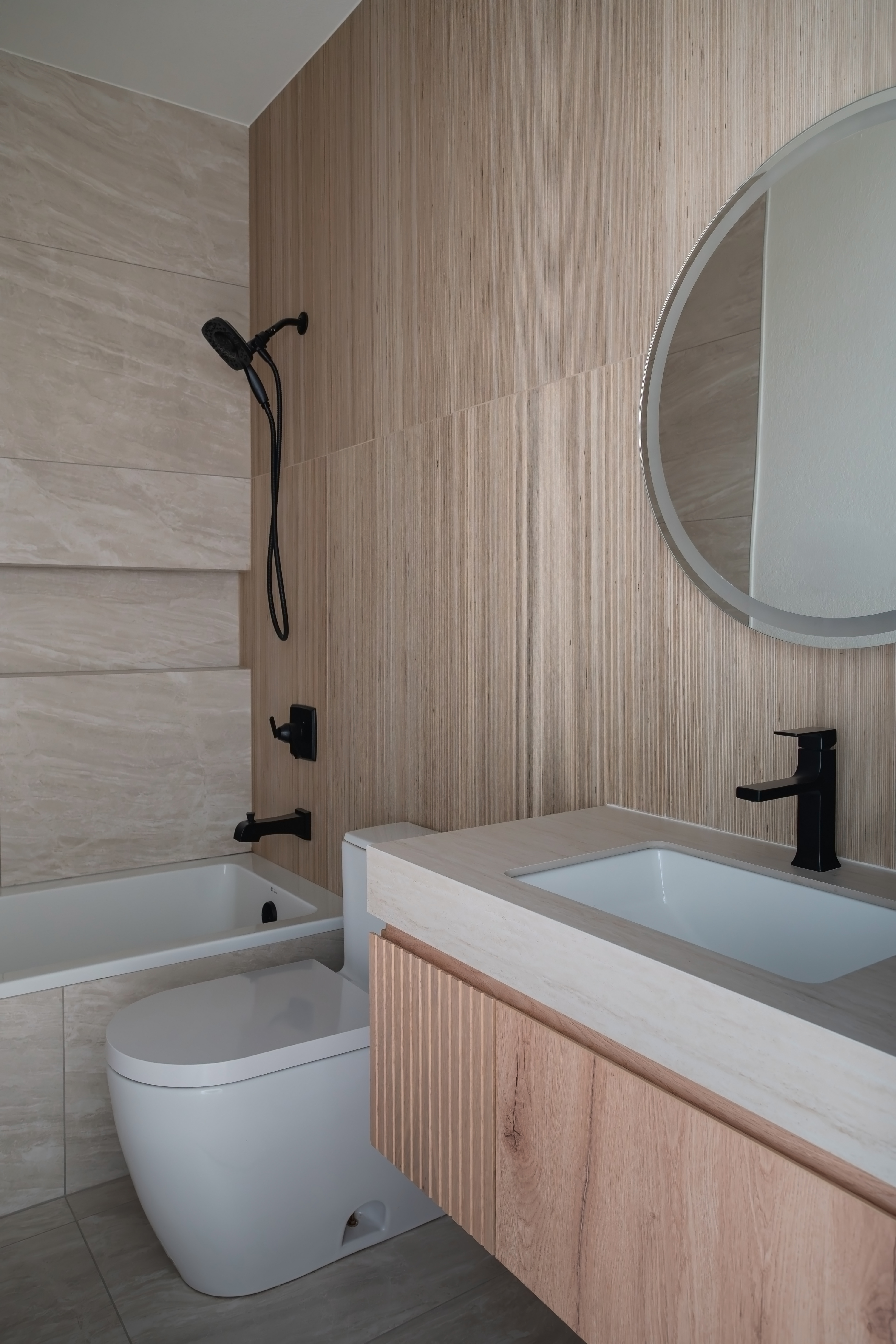 Wood-clad bathroom with tub, toilet, and round mirror