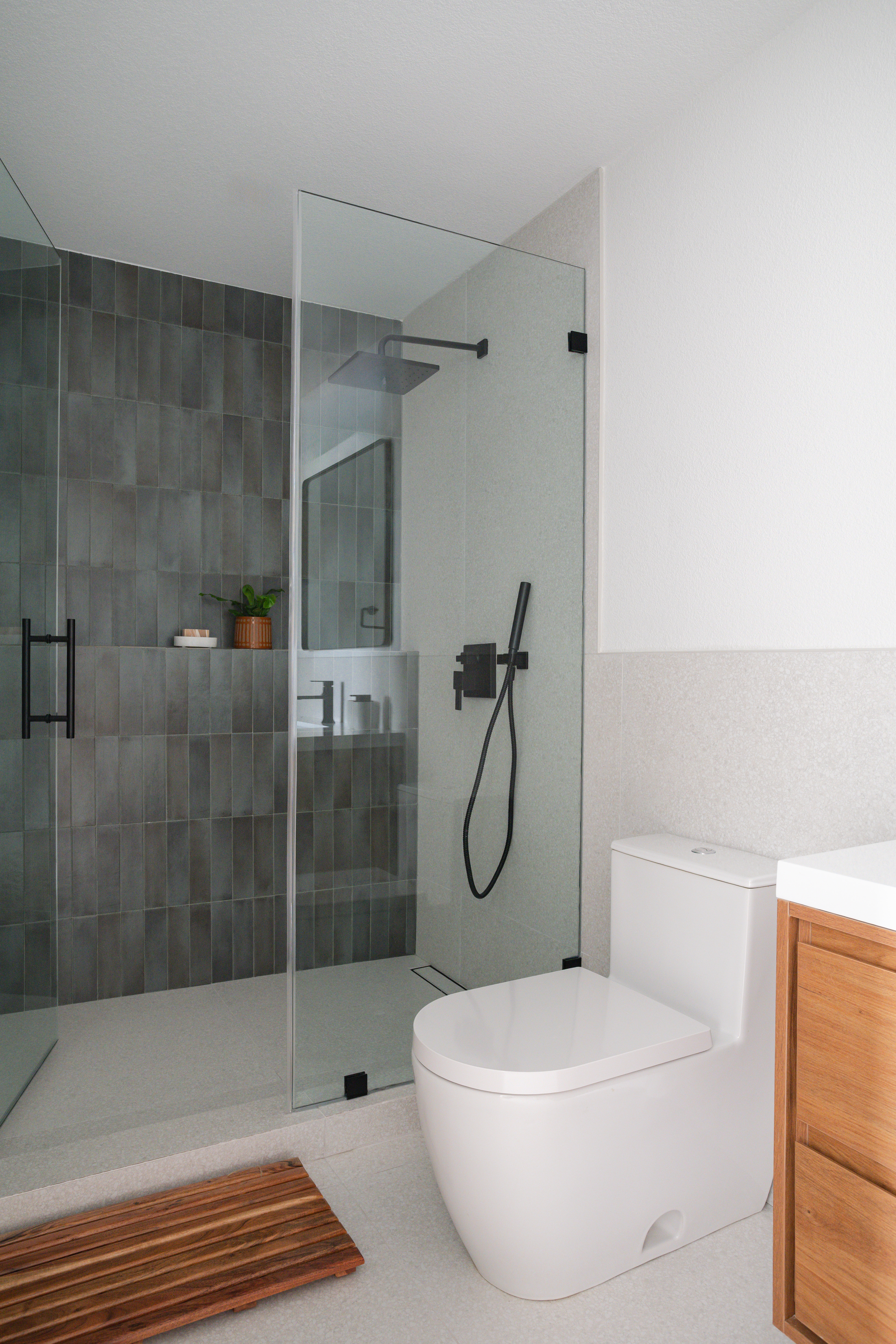 Gray zellige shower with black fixtures and teak mat